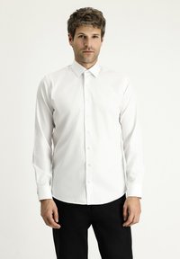 Weißes Hemd mit Knopfleiste, spitzem Kragen und langen Ärmeln. Glatte Baumwollqualität, schmale Passform, kombiniert mit dunkler Hose für Kontrast.