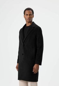 Zwarte jas van een wolblend met een reverskraag, twee knopen en zijzakken. Beschikt over een zachte textuur en een ontwerp van middellange lengte.