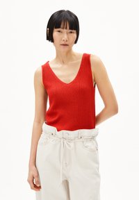 Rode geribbelde gebreide tanktop met een V-hals, gecombineerd met witte hoog-was broek met een elastische tailleband en trekkoorddetail.