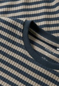 Zbliżenie na żeberkową dzianinę w granatowo-beżowe poziome paski oraz okrągłym dekolcie z granatowym wykończeniem.