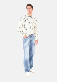 Maglione lavorato a maglia chiaro con motivo nero, abbinato a jeans in denim blu scoloriti e sneakers bianche. Il maglione presenta polsini a costine.