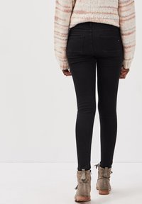 Pantalones vaqueros negros ajustados con una textura suave, de talle alto, con bolsillos traseros, combinados con botines de ante gris con detalles de borlas.