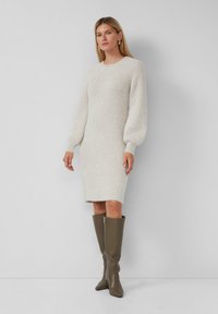 Strickkleid in Off-White mit strukturiertem Stoff, langen Puffärmeln und rundem Halsausschnitt, kombiniert mit enganliegenden olivgrünen Kniestrumpf-Stiefeln.