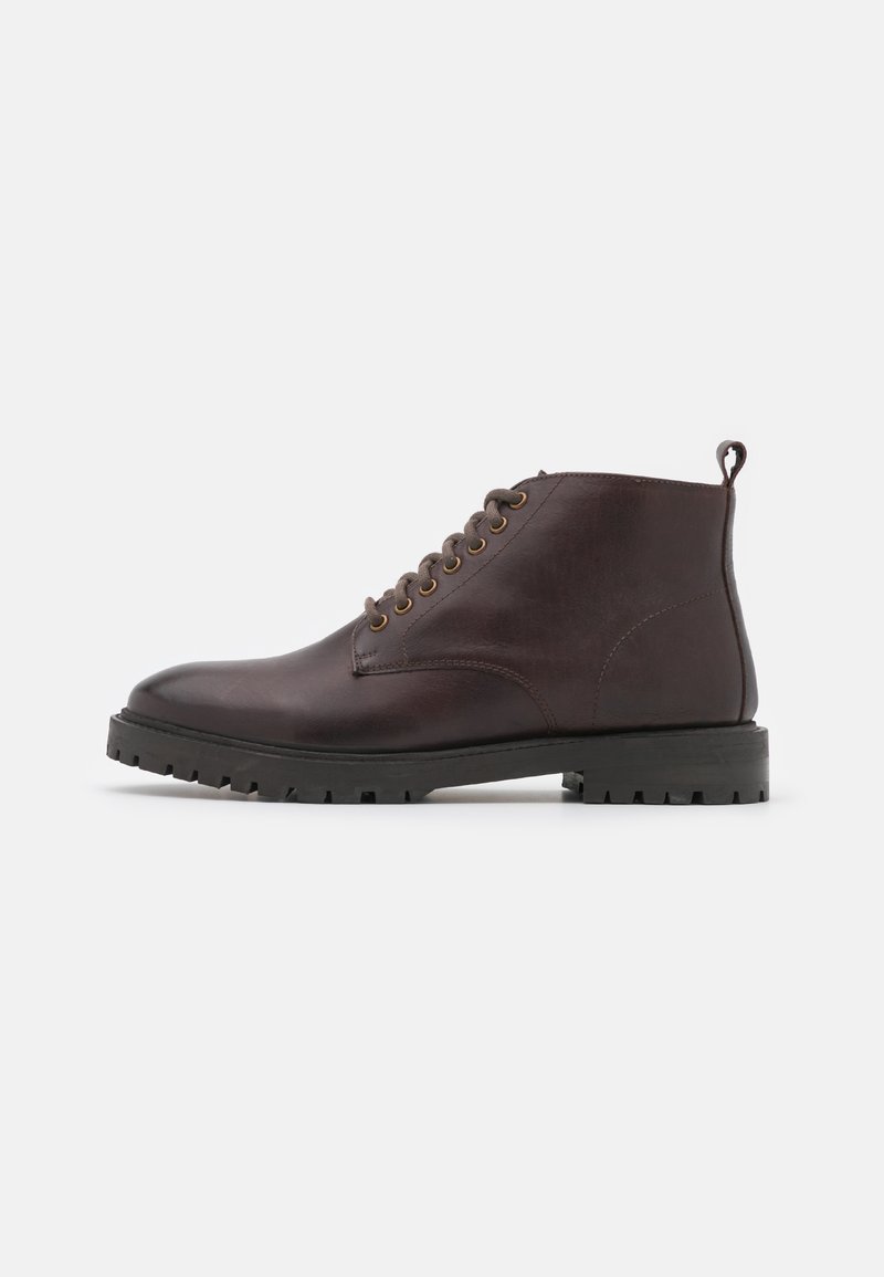 Bottine montante en cuir brun foncé avec lacets, semelle crantée noire et languette de traction sur fond blanc, vue de côté.