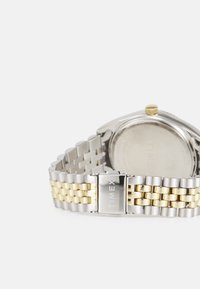 Orologio Timex con un bracciale in metallo tono argento e tono oro, caratterizzato da una cassa rotonda e un design minimalista. I link argento e oro si alternano.