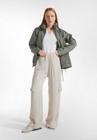 Lichtgewicht, olijfgroene jas met ritssluiting en verstelbare zoom; gecombineerd met crèmekleurige, wijde cargobroek met zijzakken en trekkoord in de taille.