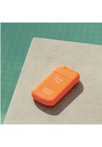 Oranger Handdesinfektionsmittelbehälter mit abgerundeten Kanten, strukturierter Silikonoberfläche, beschriftet mit "Sunset Fleur" und einem kleinen Ausgussdeckel.