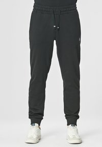 Pantaloni della tuta neri realizzati in tessuto morbido, con un cinturino elastico con cordino, tasche laterali e polsini a forma affusolata.