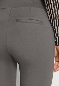 Grå leggings med ett mjukt, stretchigt material. Har bakfickor och hög midjeband. Närbild visar texturerad sidodetalj.