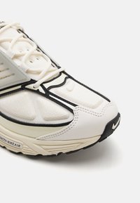 Baltie sporta apavi ar teksturētu tīkla augšpusi, melniem akcentiem un biezu zoli. Iezīmējas ar slāņotu dizainu, redzamām auklām un logotipa detaļu uz pirksta.