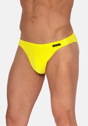 Männlicher Oberkörper mit leuchtend gelben Badehosen und einem schwarzen "olaf benz"-Label an der rechten Hüfte, einfarbiger weißer Hintergrund.