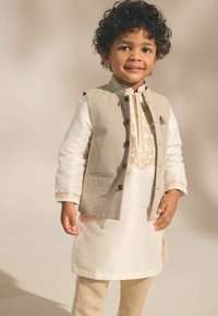 Kurta beige avec broderie dorée, superposée avec un gilet gris clair doté de boutons marron et d'une poche. Complétée par un pantalon beige.