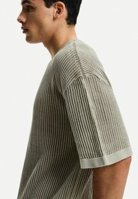 Beige knit sweater with a textured pattern, featuring short sleeves and a crew neckline. Fabric is lightweight and breathable.