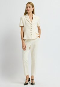 Cream blazer with short sleeves, six button closure, and two front pockets, paired with tailored cream pants and black T-strap heels.