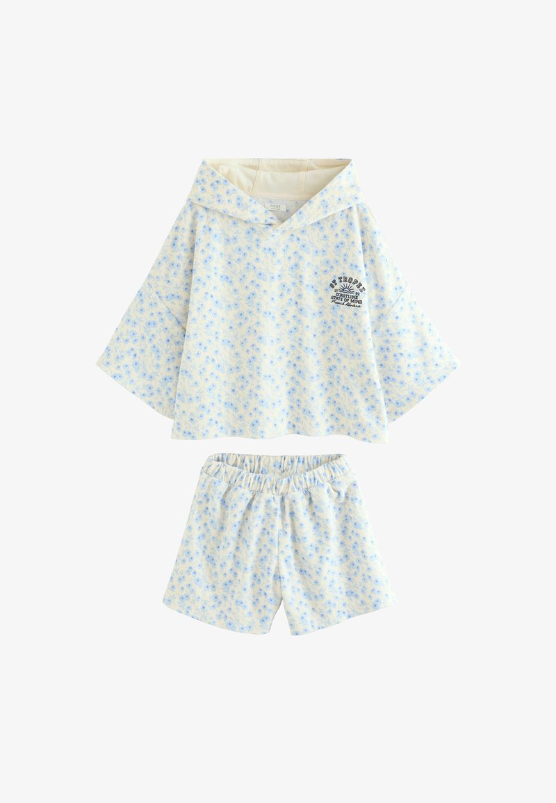 Haut à capuche crème clair et shorts à taille élastique avec un petit imprimé floral bleu et le texte noir St Tropez sur le haut côté gauche de la poitrine.