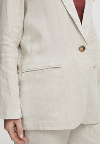Helle beige Leinenblazer mit einem Ein-Knopf-Verschluss und einem Reverskragen, ausgestattet mit einer Brusttasche und aufgesetzten Seitentaschen. Texturiertes Material.