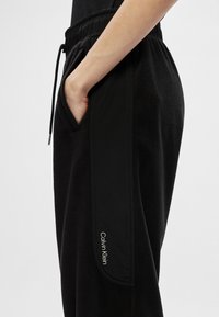 Czarne dresowe spodnie z polaru z elastycznym pasem, boczną kieszenią oraz kontrastową czarną wstawką z białym logo "Calvin Klein".