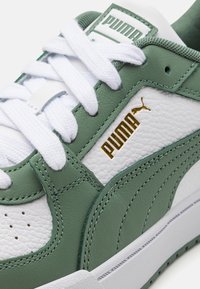 Baskets Puma blanches et vertes avec lacets blancs et logo Puma doré sur le côté, montrant des coutures détaillées et un cuir texturé.