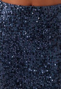 Marinblå paljetttyg med olika storlekar av runda paljetter. Blänkande och texturerad yta, tätt täckt för en glittrande effekt.