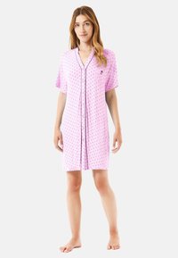Camisón corto rosa con mangas cortas, cierre frontal de botones y un pequeño logo bordado. Presenta un patrón de lunares en tonos más oscuros.