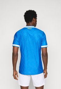 Blue athletic jersey featuring short sleeves, white accents, and a textured pattern. Back displays "RMCP" in yellow lettering.