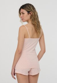 Pigiama di colore rosa chiaro con pois neri. Spalline sottili a spaghetti, canotta aderente e pantaloni shorts larghi con bordo arricciato. Texture di tessuto morbido.