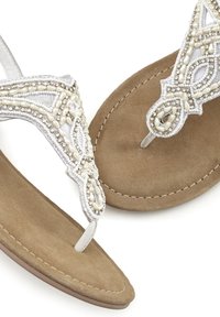 Perlenbesetzte weiße Flip-Flops mit einem strukturierten, hellbraunen Wildleder-Fußbett, das ein kunstvolles Design und silberne Akzente aufweist.