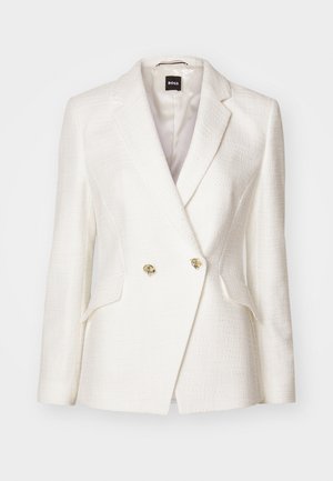 Hvit dobbeltradet blazer laget av teksturert stoff. Har gullfargede knapper, klaffelapper og to lommer foran.