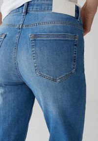 Lichtblauwe denim jeans met een gladde textuur, vijfzakken ontwerp en gestikte accenten, met een witte merklabel op de tailleband.