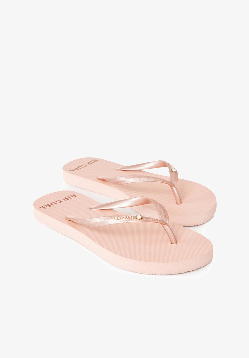 Tongs en caoutchouc rose avec des brides métalliques et une semelle texturée. Présente le logo "RIP CURL" en lettres majuscules sur la semelle.