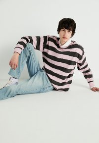 Camisa de manga larga con rayas horizontales negras y rosas, cuello redondo y corte relajado. Combinada con unos jeans de mezclilla azul claro y zapatos blancos.