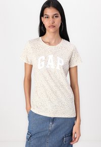 Šviesiai smėlinė marškinėliai su subtiliu leopardo raštu ir baltu "GAP" logotipu. Trumpomis rankovėmis, apvaliu iškirpimu, minkšta medvilnės tekstūra.
