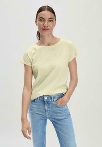 Lichtgele katoenen t-shirt met korte mouwen en een brede halslijn, gecombineerd met lichtblauwe denim spijkerbroek. Eenvoudig ontwerp, casual pasvorm.