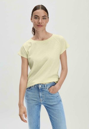 T-shirt en coton jaune clair avec manches courtes et encolure dégagée, associé à un jean en denim bleu clair. Design simple, coupe décontractée.