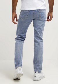 Jeans de mezclilla azul claro con un corte recto, bolsillos traseros y un sutil desgaste en forma de líneas. Combinados con zapatos deportivos blancos.