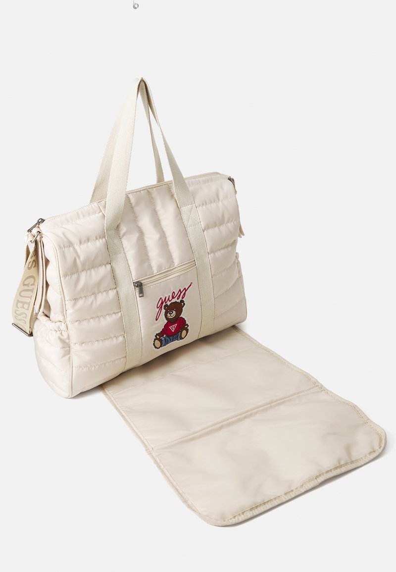 Beige quilted shoulder bag with cream straps, featuring a front pocket with a bear logo and a detachable padded base.