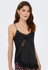 Camisole en satin noir avec des détails en dentelle complexe, des bretelles spaghetti réglables et un ourlet ondulé orné d'accents floraux.