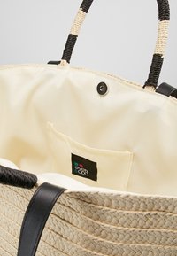 Torebka z plecionego słomy z czarnymi uchwytami, z kremowym wnętrzem i kieszonką na zewnątrz. Zawiera zapięcie na guzik oraz metkę z logo marki.