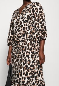 Pantonekuvatta leopardikuvioinen kietaisumekko, jossa on syvä V-pääntie, kolmanneksen pituiset hihat ja vyötäröllä solmittava nauha. Mekko on varustettu valuvalla helman muotoilulla ja koostuu mustan, ruskean ja kermaisen värin sekoituksesta.