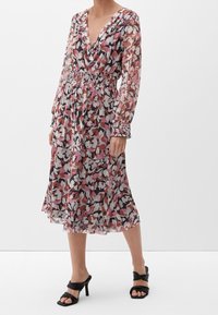 Robe midi florale en tissu transparent rose, blanc et noir. Présente un décolleté en V profond, des manches longues, une taille élastique et des poignets smockés.