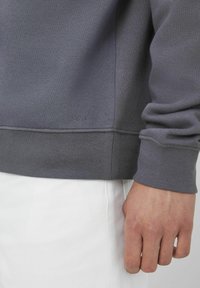 Sweatshirt gris avec un ourlet et des poignets côtelés, fabriqué en tissu doux avec une texture subtile. La marque est visible près du bas.