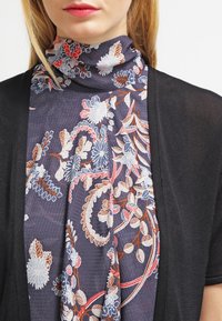 Blommönstrad scarf i mörkblått, med vita, röda och orange blommor, tillsammans med en svart, lätt cardigan. Mjuk textur.