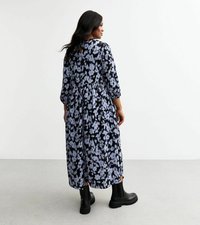 Robe florale noire et bleu clair avec des manches trois quarts, longueur genou et fentes sur les côtés. Portée avec des bottines noires.