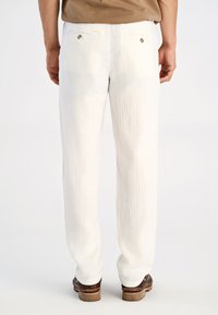 Witte katoenen broeken met een verticaal gestreepte textuur, voorzien van twee achterzakken en contrasterende hardware-accenten, gecombineerd met bruin schoeisel.