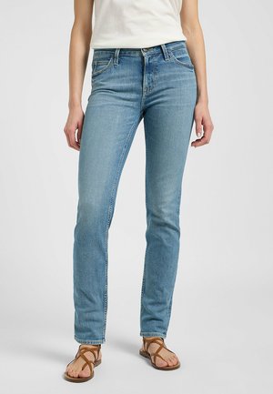 Jeans in denim azzurro chiaro con una vestibilità dritta, lievi segni di usura e design a cinque tasche, abbinati a sandali marroni con cinturini.