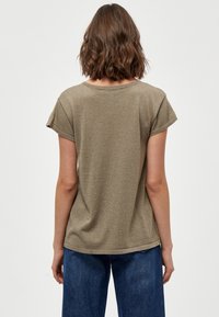Maglietta a maniche corte con scollo rotondo realizzata in tessuto testurizzato verde oliva; lucentezza sottile; orlo che si ferma all'anca, abbinata a pantaloni in denim.