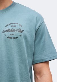 Ανοιχτό μπλε μπλουζάκι Nike με το κείμενο "Established 1972 Athletic Club Just Do It" και το λογότυπο swoosh στο αριστερό πάνω μέρος του στήθους.