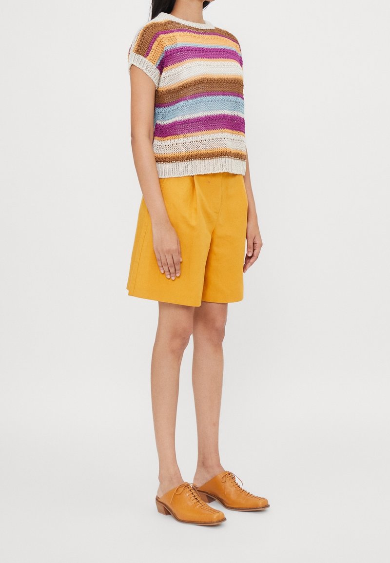 Suéter corto de punto multicolor con mangas cortas, combinado con pantalones cortos amarillos y zapatos de cuero atados color tostado, contra un fondo blanco.