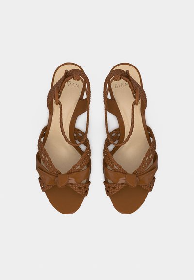 Καφέ σανδάλια ανοιχτής μύτης με πλεγμένα λουριά, θηλιές στον αστράγαλο και λεπτομέρεια κόμπου στο μπροστινό μέρος, εμφανιζόμενα από την κορυφή προς τα κάτω.