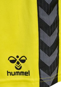 Gult stof med sort og hvid zigzag-mønsterstribe og sort hummel bi-logo og tekst nær nederst til venstre.